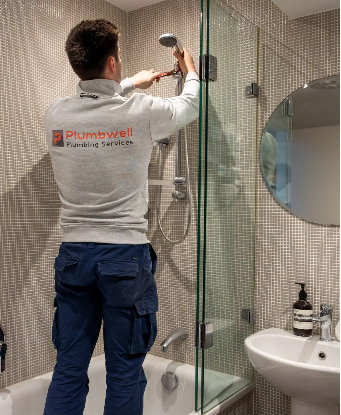 Plumber fitting a shower head in a tiled bathroom