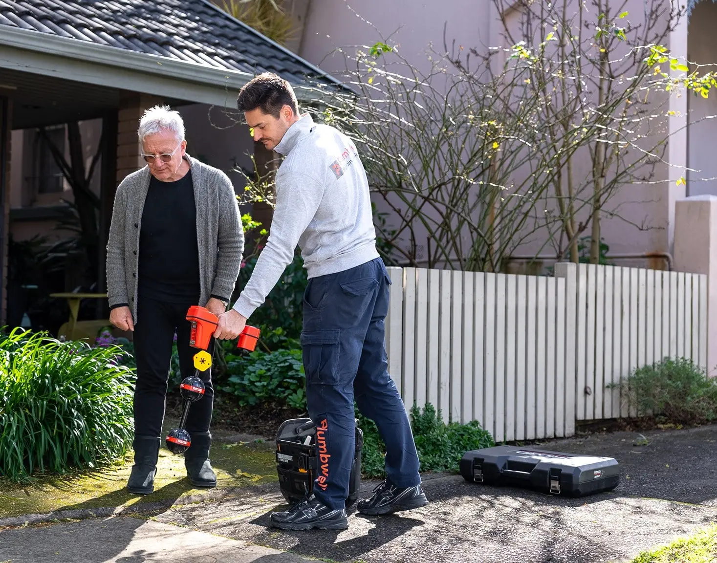 Plumber tracing a buried pipe with a locator beside the homeowner