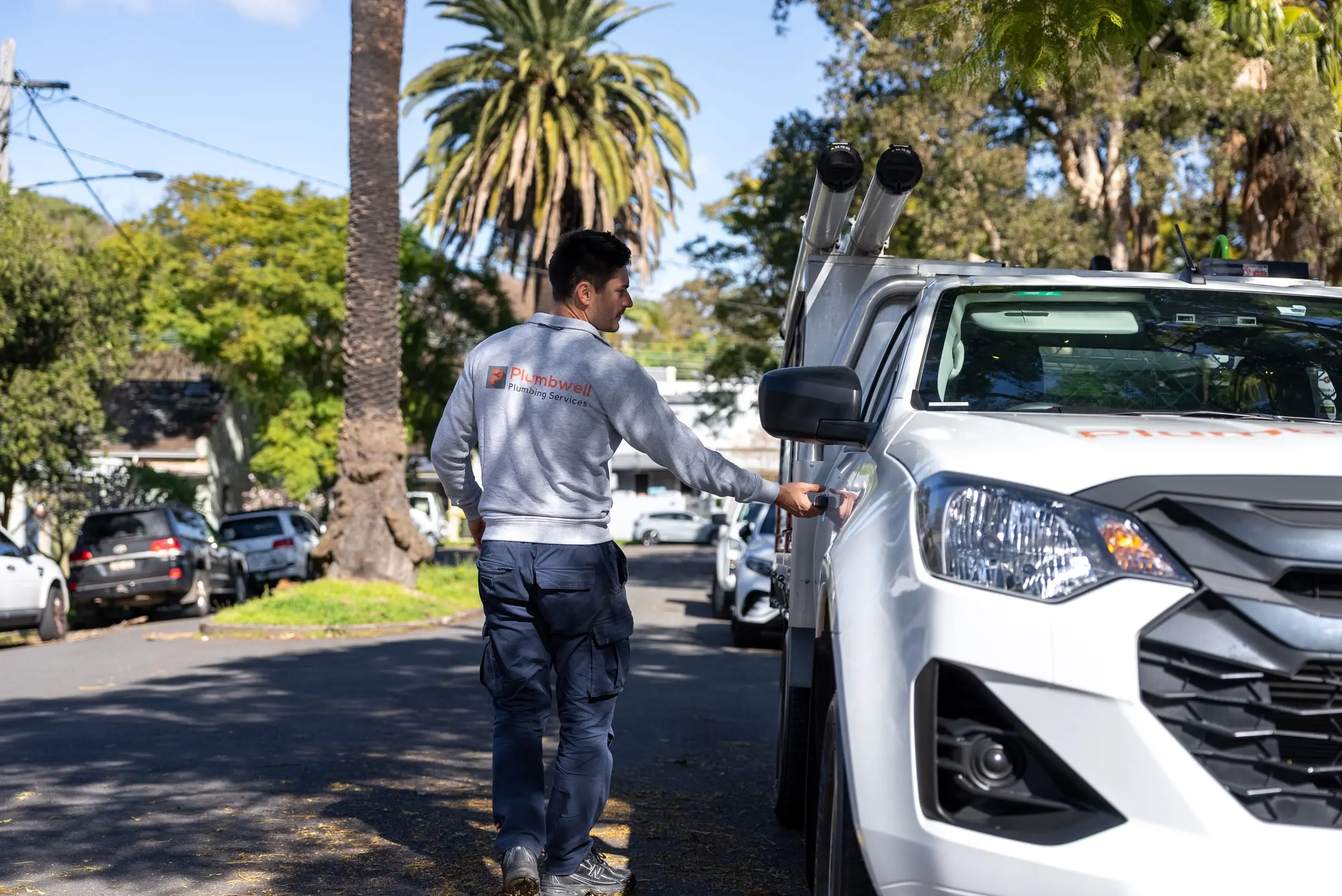 Plumber walking along a tree-lined street to his service ute