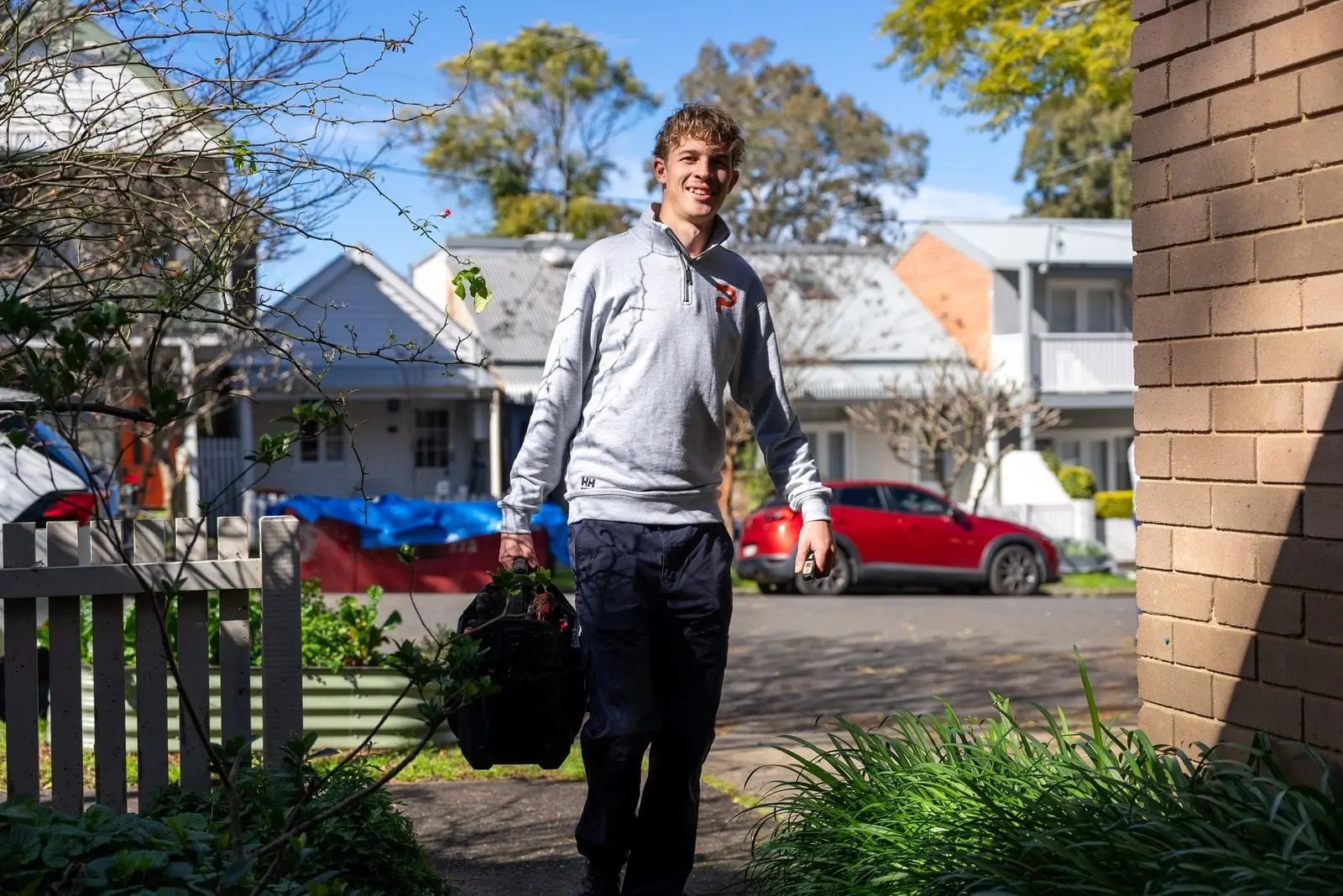 Smiling plumber walking up a front path with his tool bag
