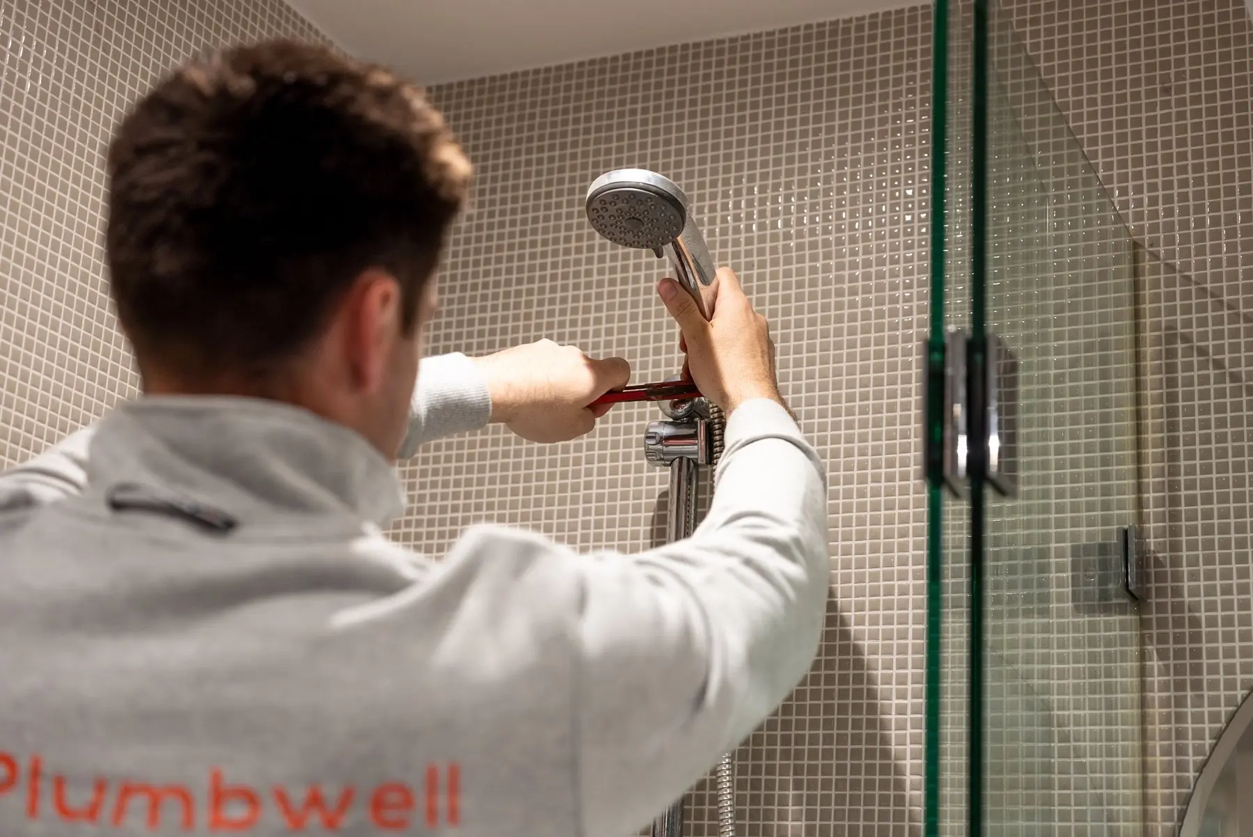 Plumber working on a shower rail and head in a tiled shower