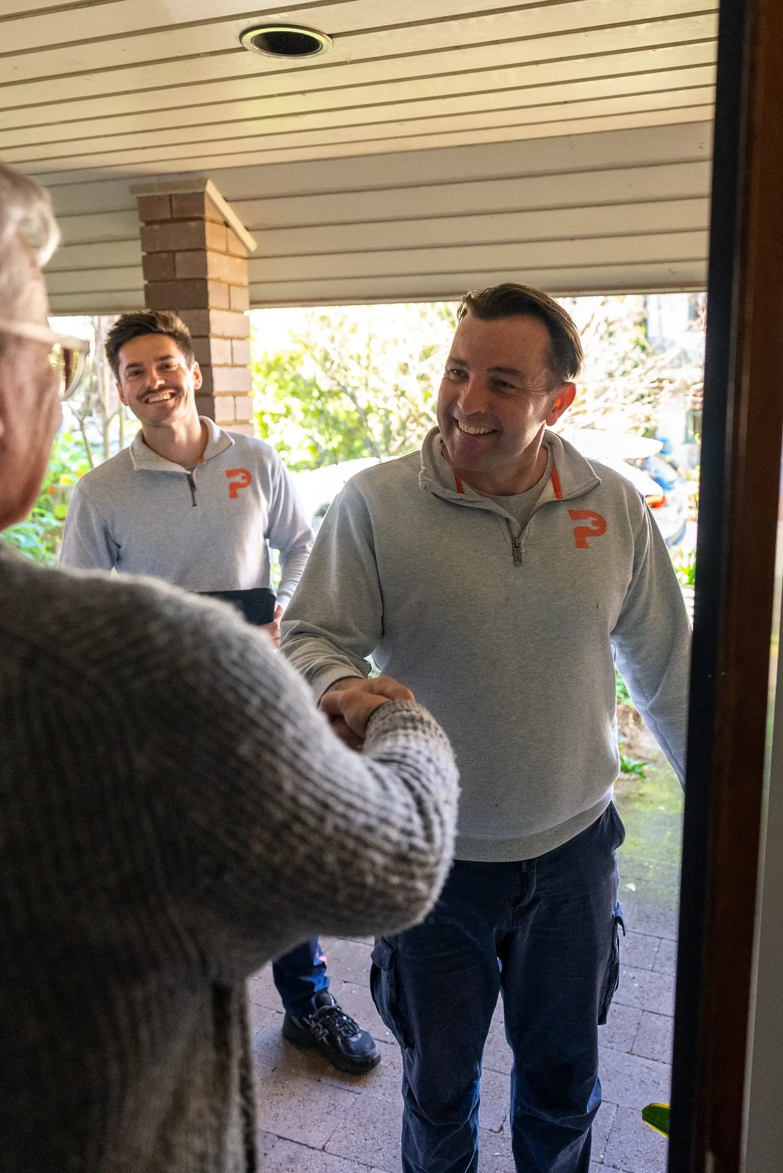 Two plumbers smiling and shaking hands with a customer at the front door