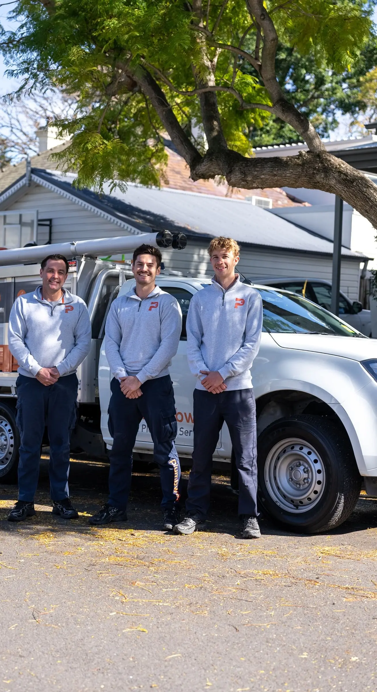 Three plumbers in branded jumpers standing in front of their service ute
